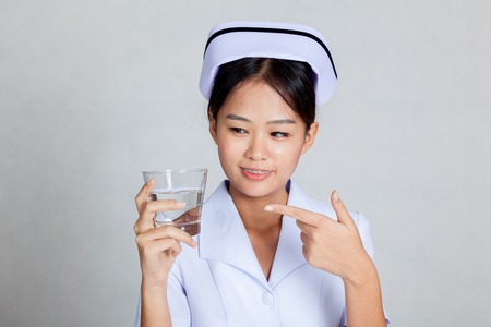Young Asian nurse point to a glass of water on gray backgroundの写真素材