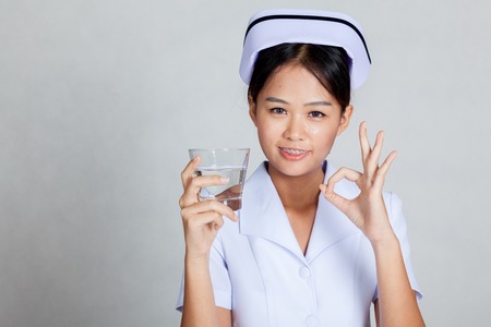 Young Asian nurse show OK with a glass of water on gray backgroundの写真素材