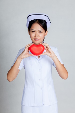 Young Asian nurse show red heart with both hand on gray backgroundの写真素材