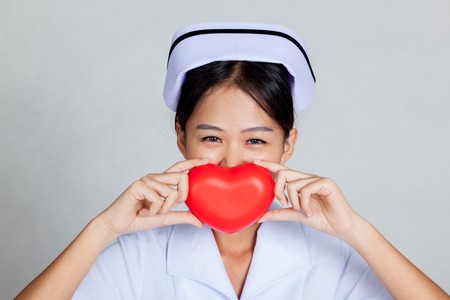 Young Asian nurse smile with red heart on gray backgroundの写真素材