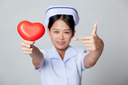 Young Asian nurse point to red heart on gray backgroundの写真素材