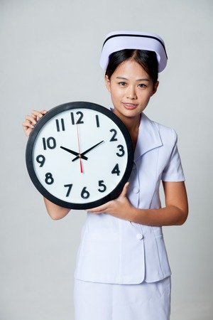 Asian young nurse with a clock on gray backgroundの写真素材