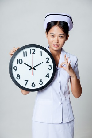 Asian young nurse show OK with a clock on gray backgroundの写真素材