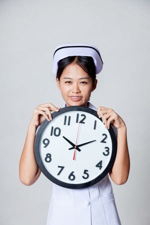 Happy time of  young Asian nurse with a clock on gray backgroundの写真素材