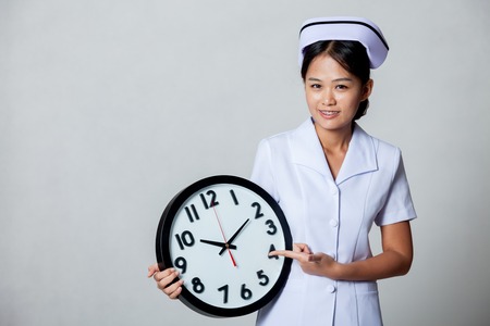 Young Asian nurse point to a clock on gray backgroundの写真素材