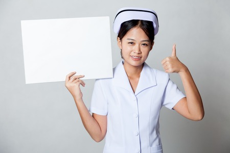 Young Asian nurse show thumbs up with blank sign on her shoulder on gray backgroundの写真素材