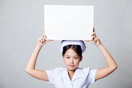 Young Asian nurse show blank sign over her head on gray backgroundの写真素材