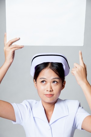 Young Asian nurse point to  blank sign over her head on gray backgroundの写真素材