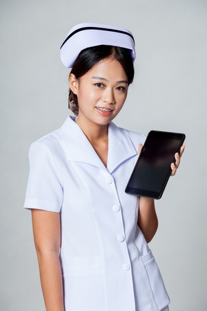 Young Asian nurse show a tablet pc on gray backgroundの写真素材