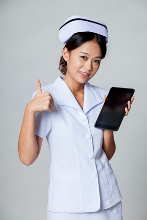 Young Asian nurse thumbs up with a tablet pc on gray backgroundの写真素材