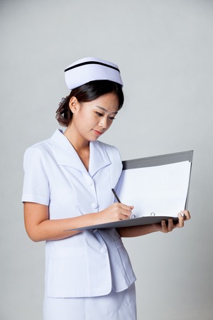 Young Asian nurse work on a folder on gray backgroundの写真素材