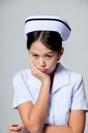 Young Asian nurse in bad mood on gray backgroundの写真素材