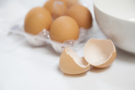 Egg shells with white bowl and carton on white backgroundの写真素材