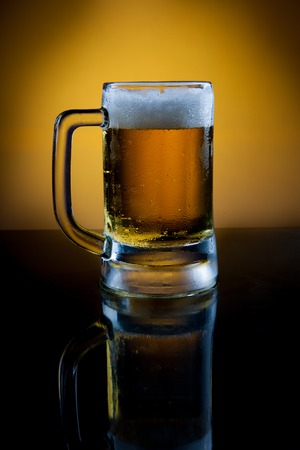 Mug of lager beer with reflection on black tableの写真素材