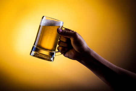 Hand hold mug of beer on gold backgroundの写真素材