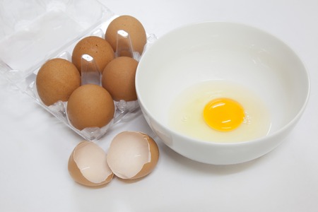 one egg yolk  in white bowl and broken egg shells on white backgroundの写真素材