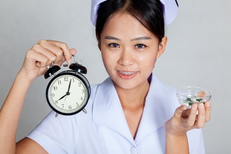Close up Asian young nurse with clock and pills on gray backgroundの写真素材