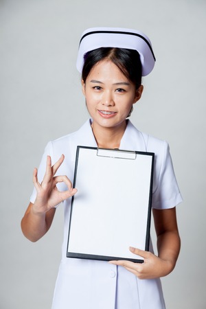 Young Asian nurse show OK  with blank paper on clipboard on gray backgroundの写真素材