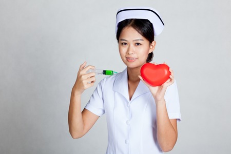 Asian young nurse hold syringe and red heart on gray backgroundの写真素材