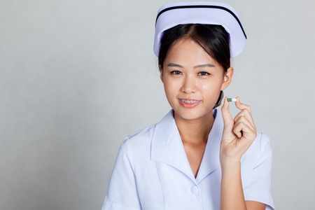 Asian young nurse show a capsule on gray backgroundの写真素材
