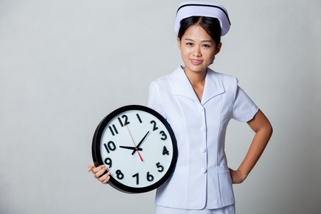 Young Asian nurse with clock on gray backgroundの写真素材