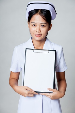 Young Asian nurse show blank paper on clipboard on gray backgroundの写真素材