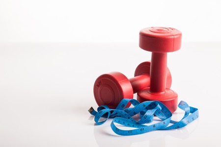 Red dumbbells weight with measuring tape for diet concept on white backgroundの写真素材