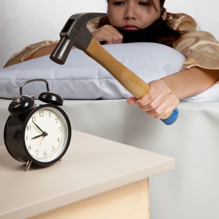 Sleepy Asian girl wake up hit alarm clock with hammerの写真素材