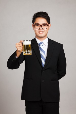 Asian businessman with mug of beer on gray backgroundの写真素材