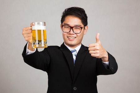 Asian businessman thumbs up with mug of beer on gray backgroundの写真素材