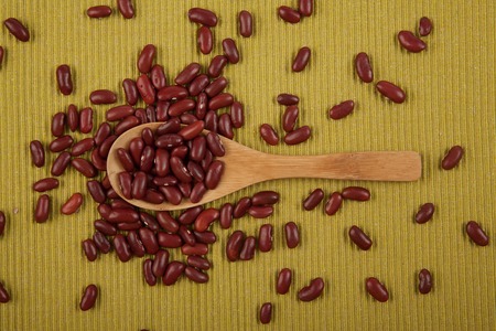 Red kidney beans with wooden spoon on green clothの写真素材