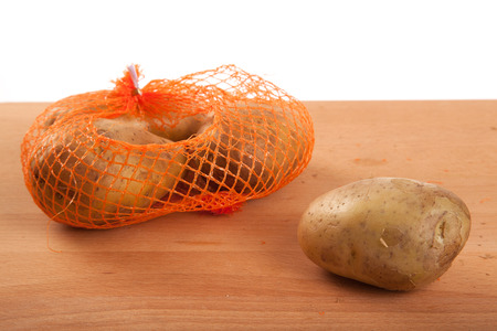 Potatoes in bag on wooden table on white backgroundの写真素材