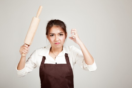 Asian Baker woman  in apron  with wooden rolling pin on gray background