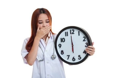 Young Asian female doctor yawn with a clock  isolated on white background.