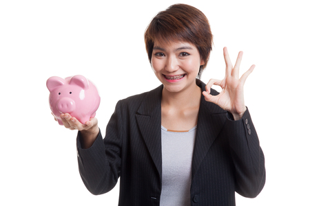 Asian business woman show OK  with pig coin bank  isolated on white background.の写真素材
