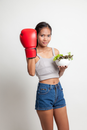 Young Asian woman with boxing glove and salad on white backgroundの写真素材