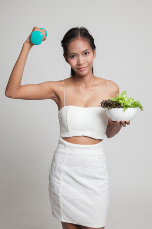 Healthy Asian woman with dumbbells and salad  on gray backgroundの写真素材