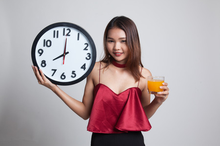 Asian woman with a clock drink orange juice on gray backgroundの写真素材