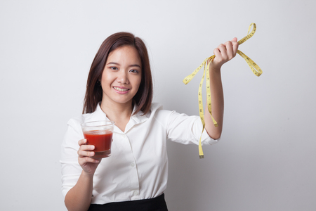 Young Asian woman with tomato juice and measuring tape on white backgroundの写真素材
