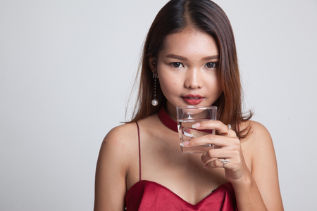 Young Asian woman with a glass of drinking water on gray background