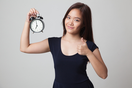 Young Asian woman show thumbs up with a clock on gray backgroundの写真素材