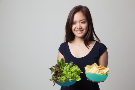 Young Asian woman with potato chips and salad on gray backgroundの写真素材