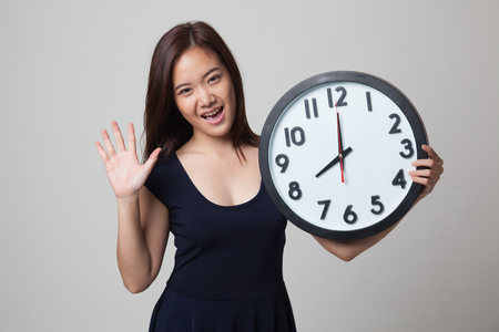 Happy Young Asian woman with a clock on gray backgroundの写真素材