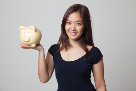 Young Asian woman with a pig coin bank on gray backgroundの写真素材