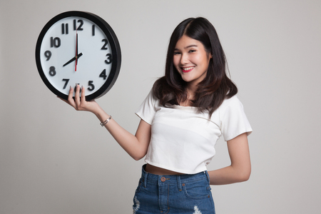 Young Asian woman with a clock on gray backgroundの写真素材