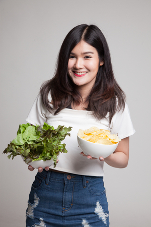Young Asian woman with potato chips and salad on gray backgroundの写真素材