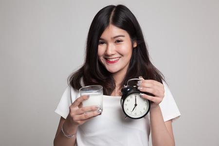 Healthy Asian woman drinking  glass of milk hold clock on gray backgroundの写真素材