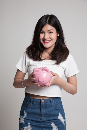 Young Asian woman with a pig coin bank on gray backgroundの写真素材