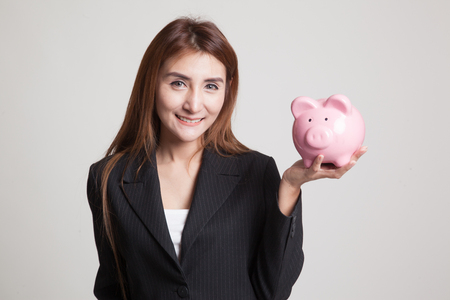 Young Asian woman with a pig coin bank on gray backgroundの写真素材