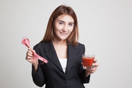 Young Asian woman with tomato juice and measuring tape on gray backgroundの写真素材